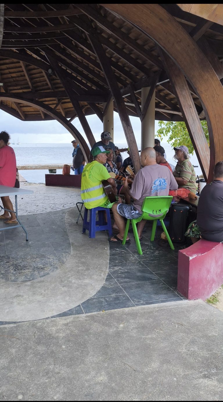 Scène de vie en Polynésie, des habitants discutent et jouent de la musique sous un abri en bord de lagon